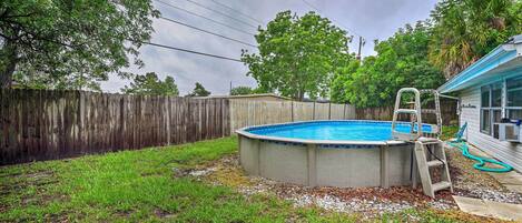 A backyard with a swimming pool, a wooden fence, and a ladder leading to the pool.
