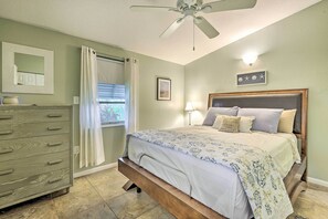 Un dormitorio con una cama, un tocador, un ventilador de techo, una ventana con cortinas y un aplique de pared.