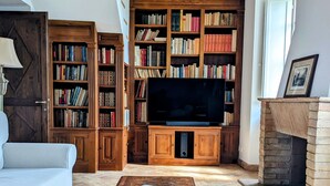 Een gezellige woonkamer met een houten plafond, een grote boekenkast, een televisie en een open haard.
