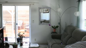 Ein Wohnzimmer mit einer Schiebetür zu einer Terrasse, einem grauen Sofa, einem Spiegel mit dekorativem Rahmen und einer hohen Stehlampe.