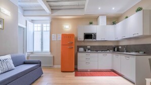 A modern kitchen with white cabinets, a grey sofa, and an orange refrigerator. - Spacious apartment on the first floor, recently renovated, modernly furnished, consisting of two double bedrooms, two complete bathrooms, sofa bed for 2 guests and single bed in the living room. It can comfortably accommodate up to 7 people. WLAN, air con (Firenze)