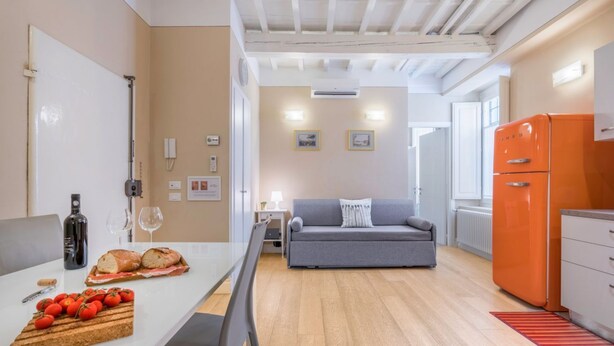 A modern kitchen with a dining area, a grey sofa, and an orange refrigerator. - Spacious apartment on the first floor, recently renovated, modernly furnished, consisting of two double bedrooms, two complete bathrooms, sofa bed for 2 guests and single bed in the living room. It can comfortably accommodate up to 7 people. WLAN, air con (Firenze)