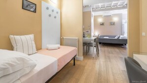 Une chambre à coucher comprenant un lit, une table de chevet, un radiateur et donnant sur un coin repas avec une table et des chaises.