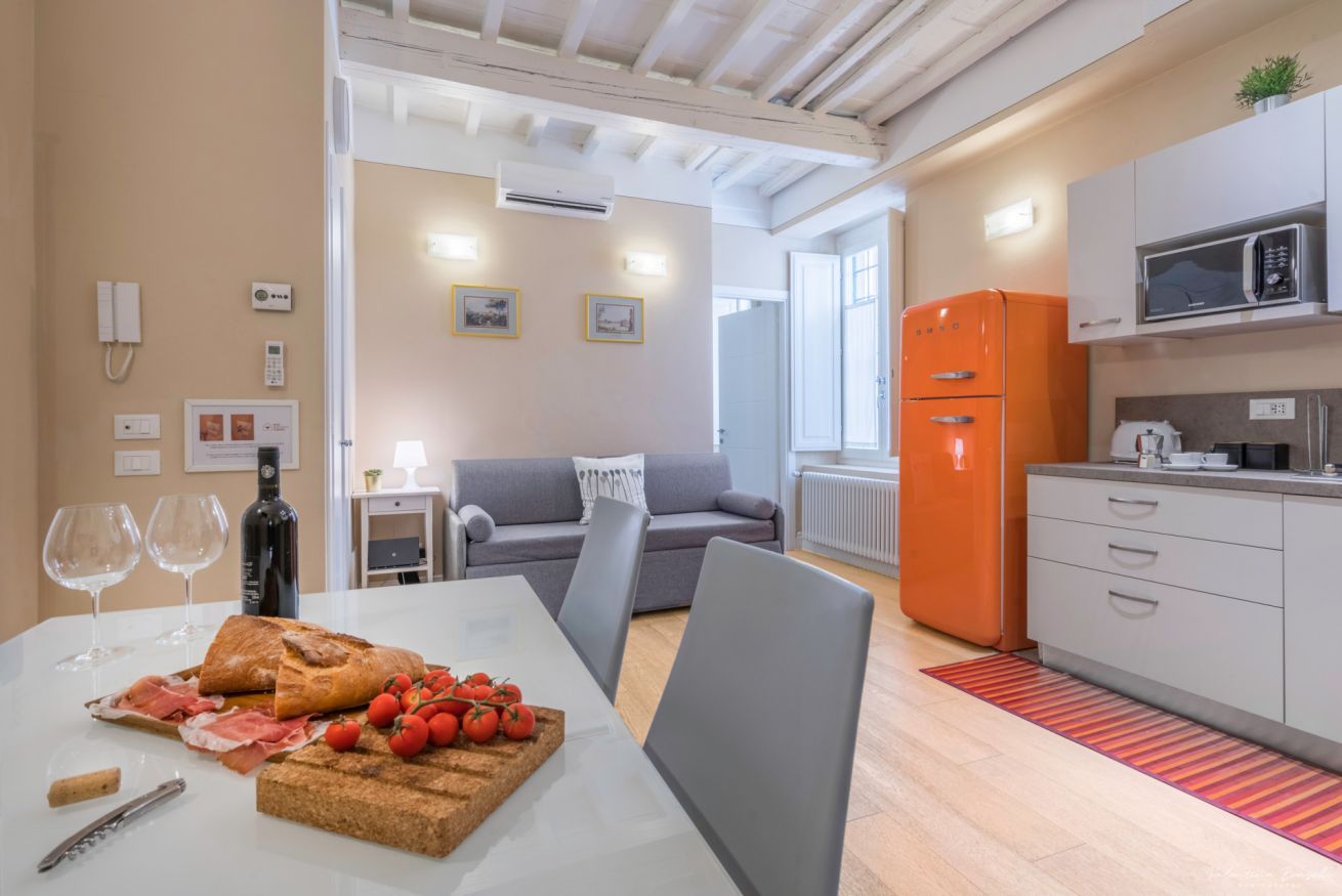 A modern kitchen with an orange refrigerator, a microwave, and a dining area with a table set for a meal.