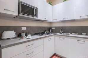 Una cocina moderna con armarios blancos, un microondas, una estufa a gas, un tostador y un lavamanos.