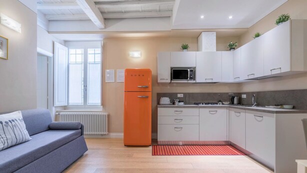 Une cuisine moderne avec des meubles blancs, un canapé gris et un réfrigérateur orange.