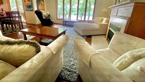 A spacious living room with a large window, a dining area with a table and chairs, and a cozy seating area with a fireplace.