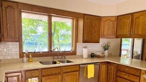 A kitchen with wooden cabinets, a stainless steel sink, and a view of a lake through large windows.