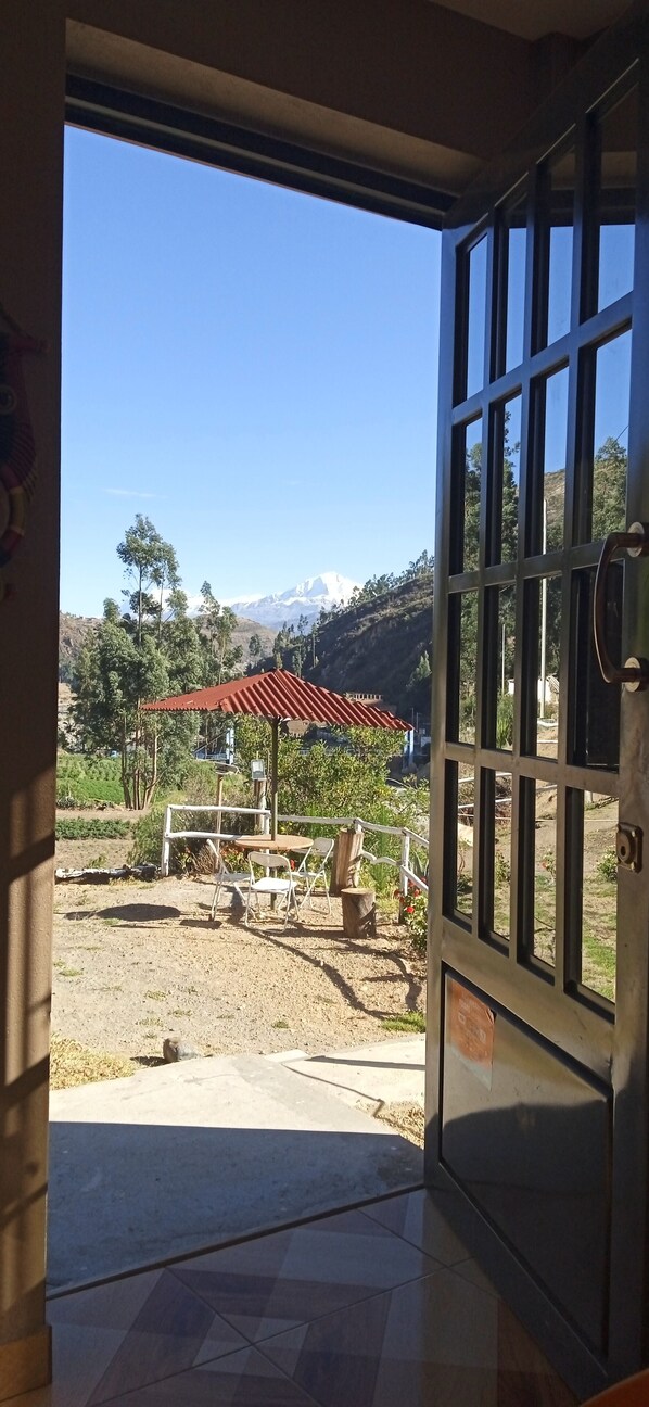 An open door leading to a patio with a view of a mountain and a red-roofed structure.