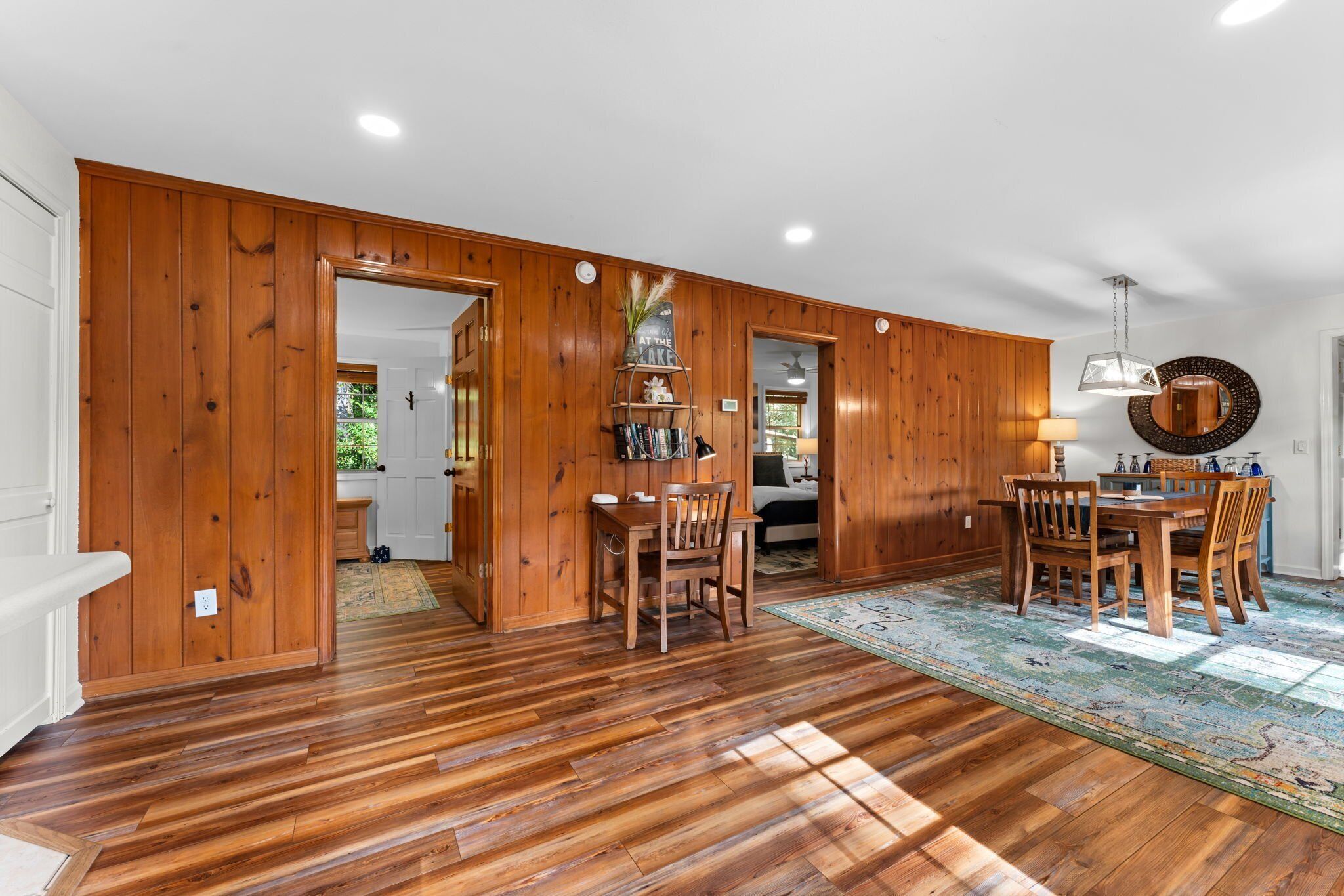 A spacious room with wooden walls and floors, a dining area with a table and chairs, and a kitchen visible through an open doorway.