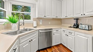 Una cocina moderna con armarios blancos, electrodomésticos de acero inoxidable y una ventana con vistas a árboles.