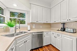 Una cocina moderna con armarios blancos, electrodomésticos de acero inoxidable y una ventana con vistas a árboles.