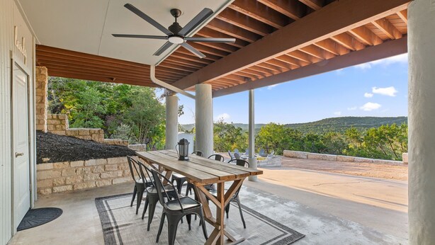 Un patio exterior con mesa y sillas, un ventilador de techo y vistas al paisaje.