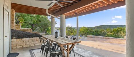 Un patio exterior con mesa y sillas, un ventilador de techo y vistas al paisaje.