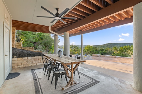 Un patio exterior con mesa y sillas, un ventilador de techo y vistas al paisaje.
