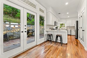 A spacious kitchen with white cabinetry, a wooden floor, and a stone wall outside.