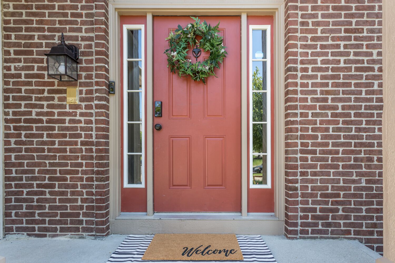 A red door with a wreath, a mailbox, and a welcome mat.