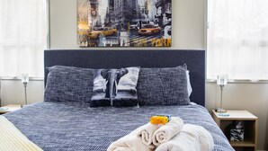 A hotel room with a large bed, a cityscape painting on the wall, and a nightstand with a lamp. - Chic Private Studio Close to Airport, Bus & Shops - Breakfast included (Christchurch)