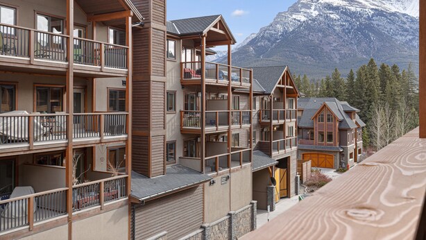 Un hotel de varios pisos con balcones, fachada de piedra y montañas al fondo.