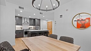 Una cocina moderna con armarios grises, una mesa de comedor de madera y una lámpara de araña.