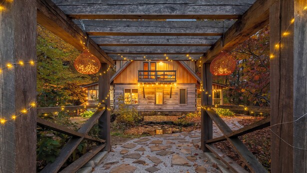 Ein rustikales Holzhaus mit einem Steinweg, der zum Eingang führt, umgeben von Bäumen und Lichterketten.