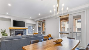 A modern living room with a fireplace, grey sofa, wooden dining table, and a TV mounted on the wall.
