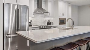 A modern kitchen with stainless steel appliances, white cabinetry, a central island with bar stools, and a microwave.