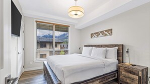 Een slaapkamer met een groot bed, een houten nachtkastje, een aan de muur bevestigde televisie en een raam met blinds.