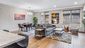 Un salon moderne avec un canapé gris, une table à manger avec des chaises et une grande fenêtre équipée de stores.