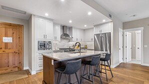 Une cuisine moderne avec des meubles blancs, un réfrigérateur en acier inoxydable et un îlot central doté de tabourets de bar.