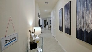 A hallway with a welcome sign, a horse sculpture, and abstract paintings on the walls. - Solara 7BR/6.5BA Villa w/Pool/Spa, 3544 sqft, Sleeps 18, Lake and green view. (Reunion)