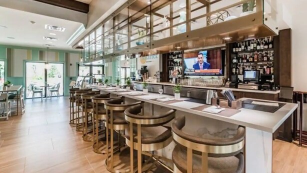 A modern bar area with a long counter, multiple stools, and a television screen. - Solara 7BR/6.5BA Villa w/Pool/Spa, 3544 sqft, Sleeps 18, Lake and green view. (Reunion)