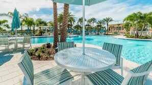 A poolside area with a round table and chairs, surrounded by palm trees and a clear blue sky. - Solara 7BR/6.5BA Villa w/Pool/Spa, 3544 sqft, Sleeps 18, Lake and green view. (Reunion)