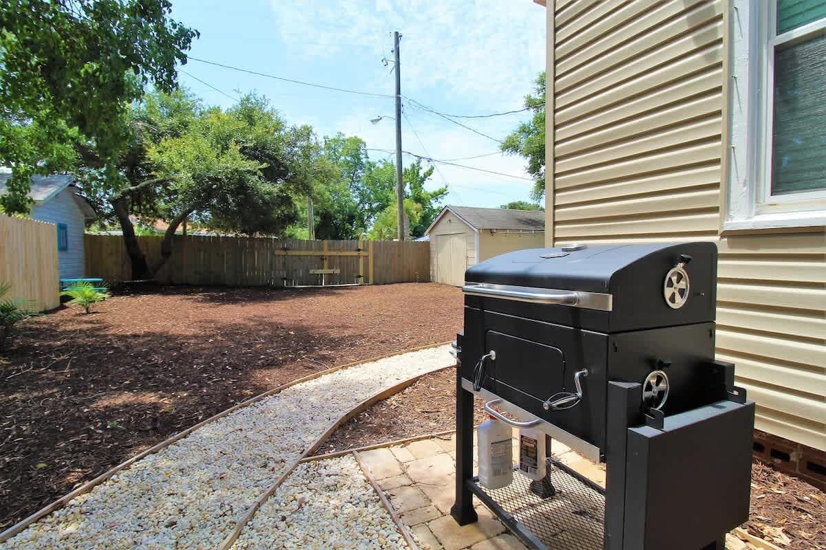 Un barbecue dans un jardin, avec une clôture en bois, un abri de jardin et une maison en arrière-plan.