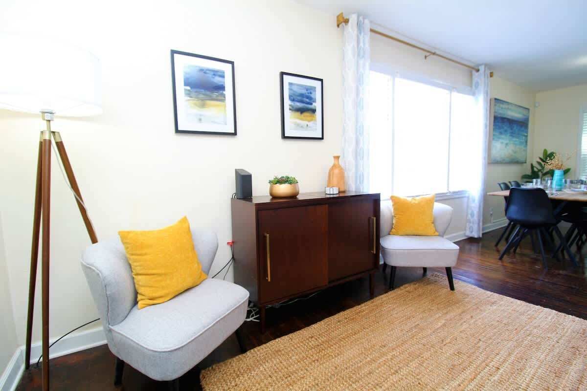 A living room with a sofa, a cabinet, a dining table with chairs, and framed pictures on the wall.