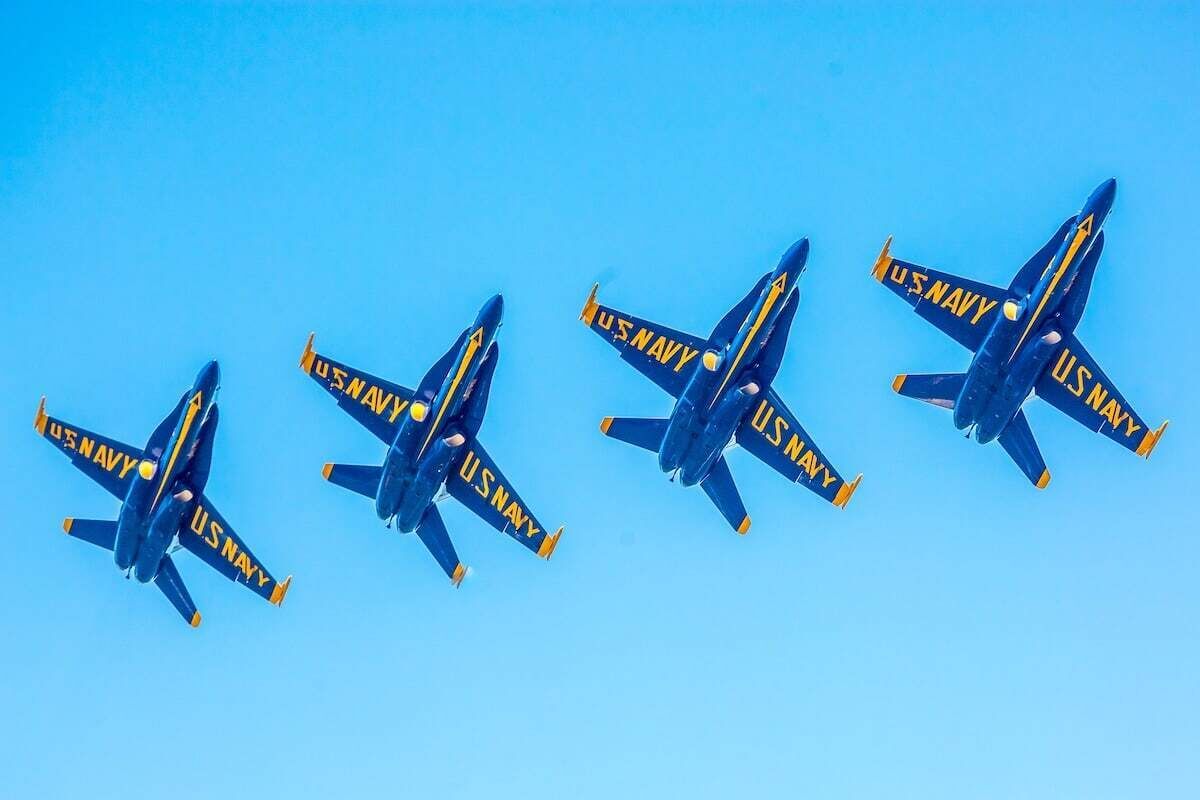 Vier US Navy Flugzeuge in Formation vor blauem Himmel.