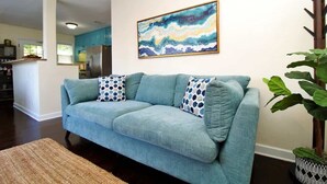 Una sala de estar con un sofá azul, un cuadro y una planta en maceta.