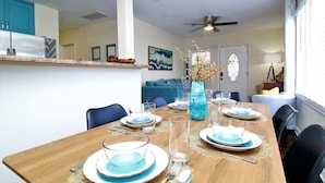 Un comedor con una mesa de madera dispuesta para cuatro, sillas y un florero con ramas.