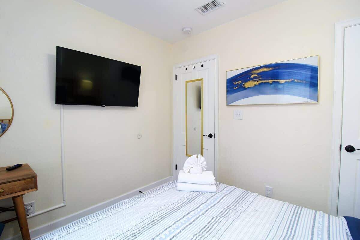Ein Schlafzimmer mit einem Bett, einem Flachbildfernseher, einer Tür mit Spiegel und einem Bild an der Wand.