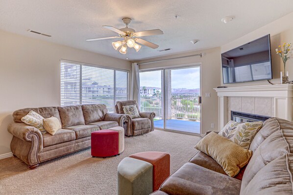 A living room with a ceiling fan, a fireplace, and a large window with a view.