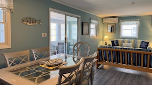 A dining area with a glass-top table, chairs, and a bowl of fruit. There is a sofa with striped cushions in the background. - Broadkill Beach House- Dog Friendly! Sleeps 13 (Milton)