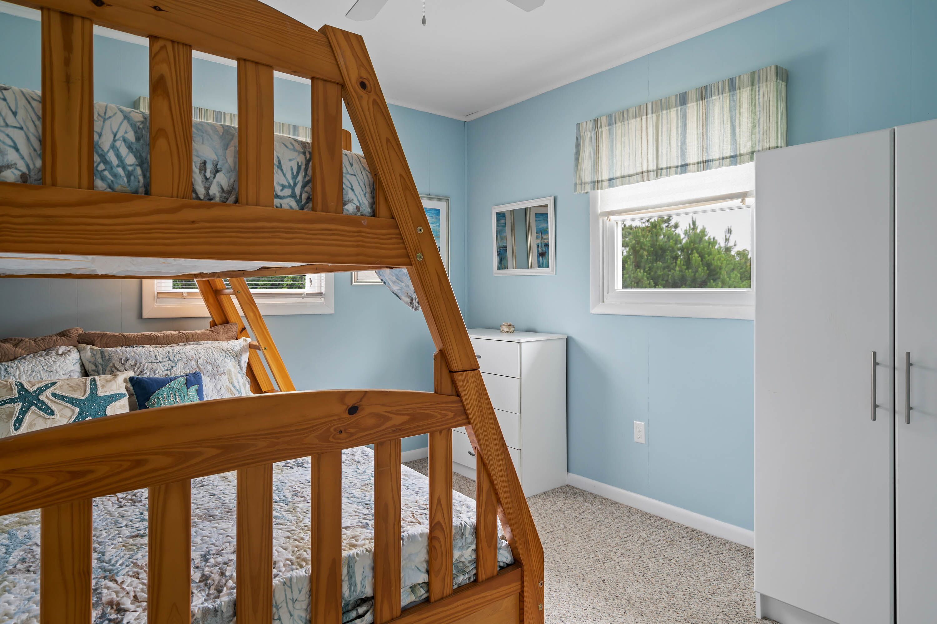 Ein Zimmer mit einem Etagenbett, einem weißen Schminktisch, einem Fenster mit Aussicht und einem Deckenventilator.