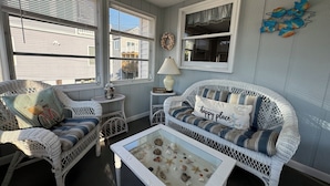 A cozy living room with wicker furniture, a glass coffee table with seashells, and a view of the neighborhood. - Broadkill Beach House- Dog Friendly! Sleeps 13 (Milton)