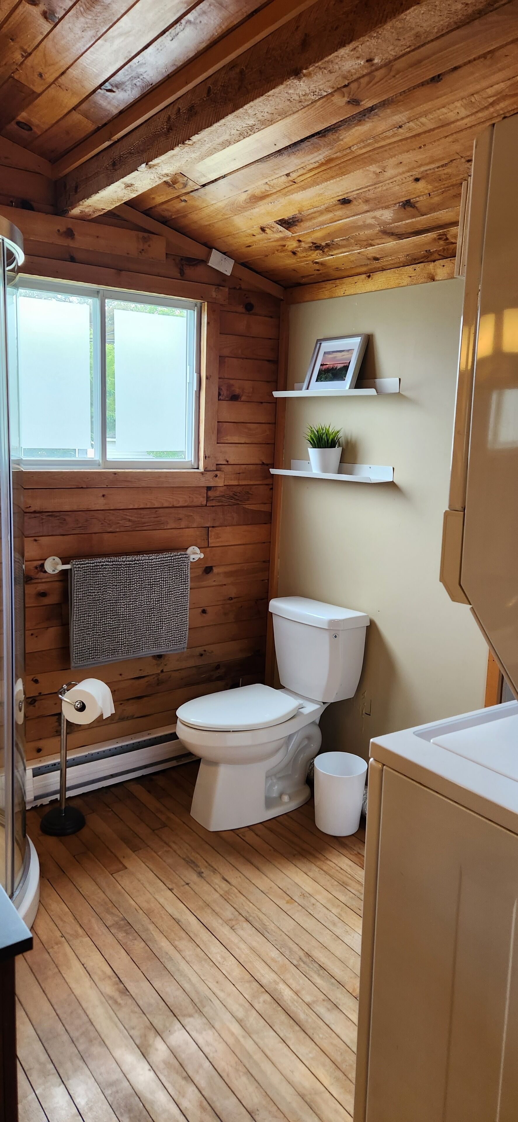 A wooden cabin bathroom with a toilet, sink, and a window.