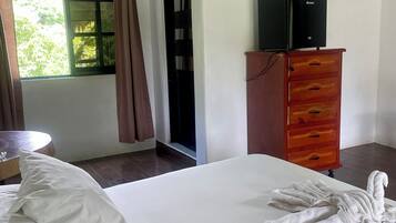 A hotel room with a bed, a wooden dresser, a small table, and a window with curtains.