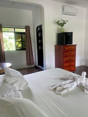 A hotel room with a bed, a wooden dresser, a small table, and a window with curtains. - Villa del Mar (San Pedro Pochutla)