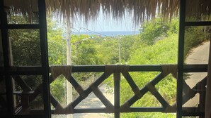 A room with a view of a lush green landscape through a large glass door. - Villa del Mar (San Pedro Pochutla)