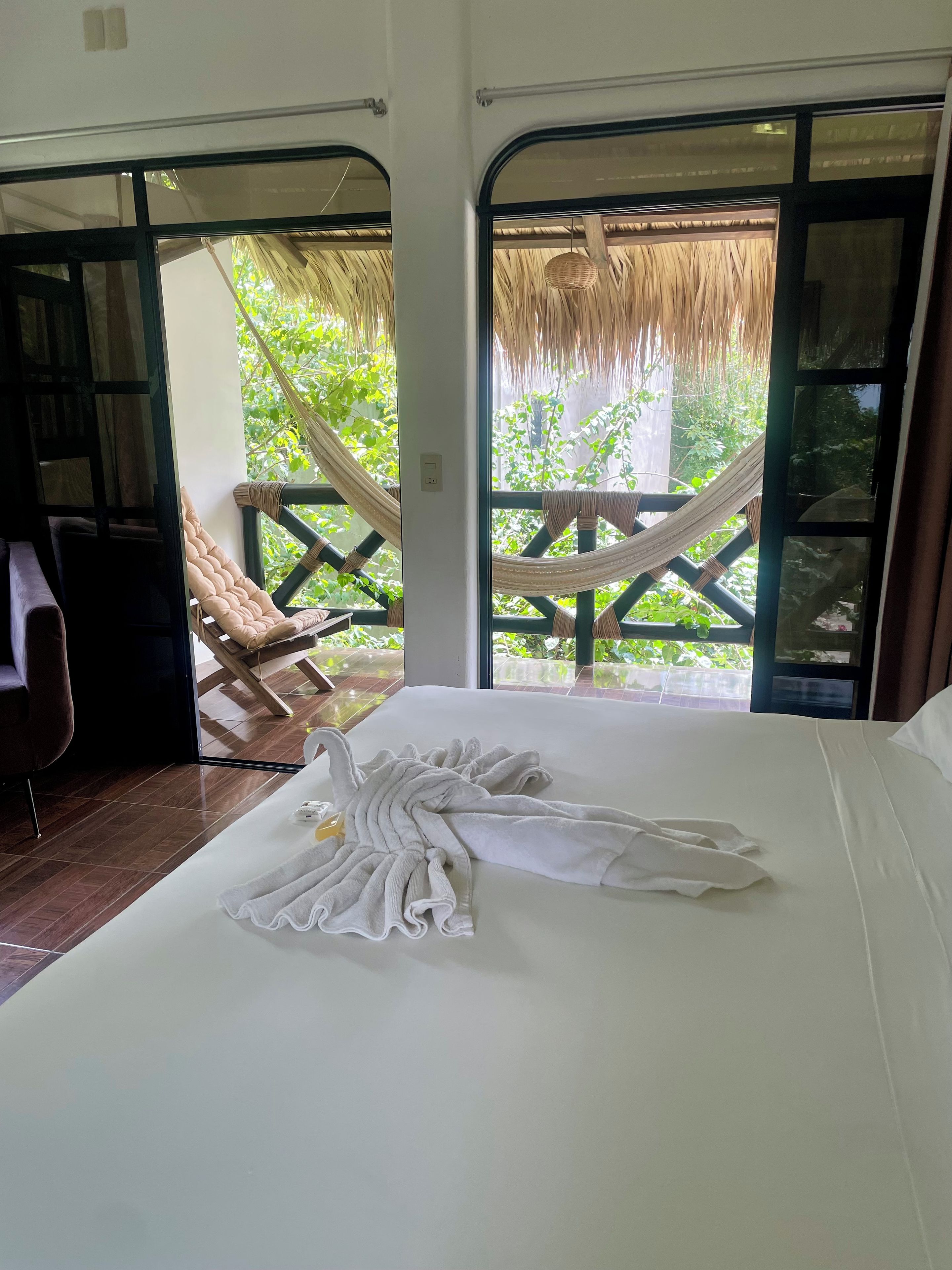 A room with a bed, a hammock, and a view of greenery outside.
