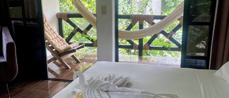 A room with a bed, a hammock, and a view of greenery outside.