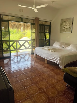 Quarto com cama, ventilador de teto, janela com vista para o verde e chão estampado.